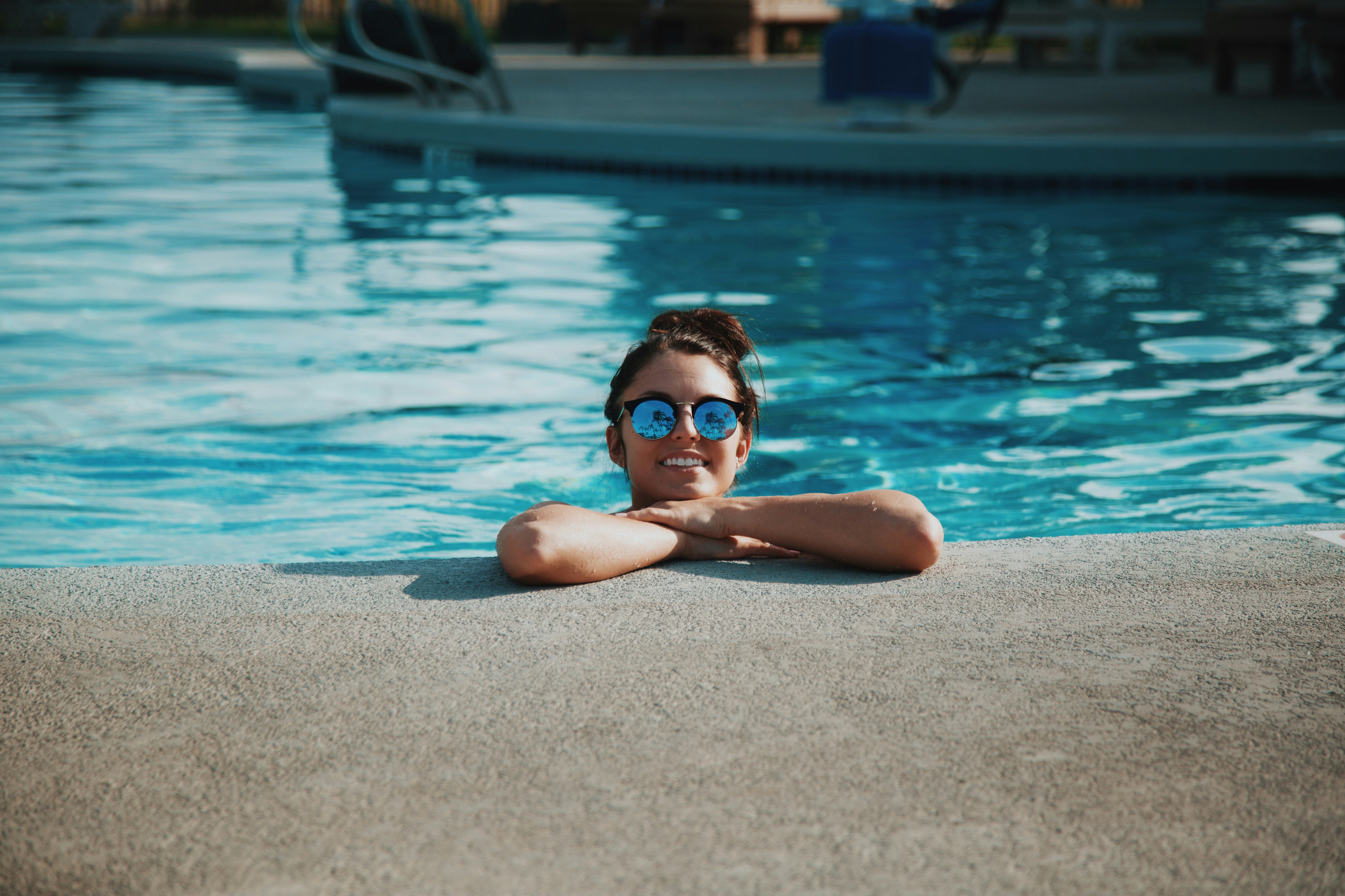 jeune fille avec des lunette de soleil dans une piscine et accoudée sur le bord
